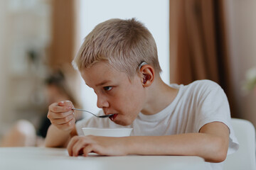 A boy with hearing aids enjoys a healthy breakfast, showcasing inclusive daily routines and...