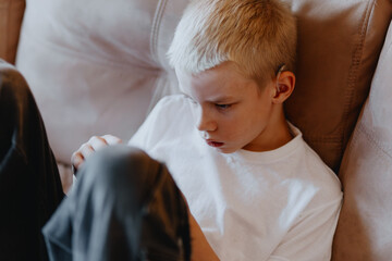 A blond boy with hearing aids gazes thoughtfully in a portrait celebrating inclusive beauty....