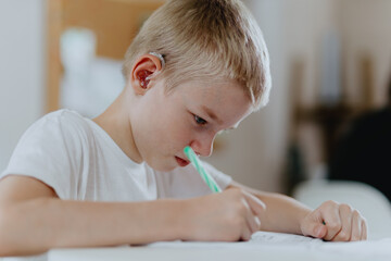 A boy with hearing aids focuses on homework, showcasing natural inclusive education. Authentic...