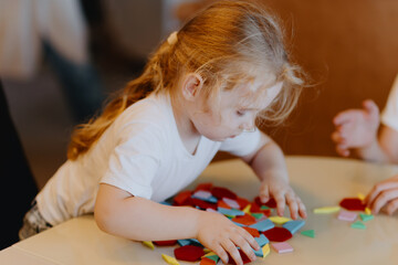 A brother with hearing aids and his 3-year-old sister play together with building blocks and board...
