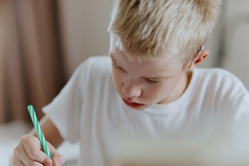 A boy with hearing aids focuses on homework, showcasing natural inclusive education. Authentic...