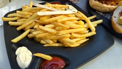 Golden fries stacked symphonically on a black platter, savory symphony of emulsified condiments, perfect for Fryday indulgence