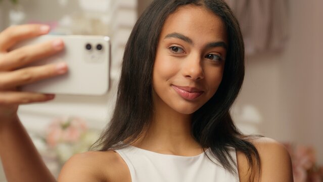 Hispanic woman beauty blogger photograph in home bathroom photo selfie mobile phone camera blog vlog internet social media cosmetics makeup fashion influencer Latina girl female celebrity hairstyle