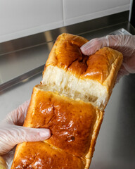 Gloved hands tearing fluffy brioche under industrial glow, evoking buttery warmth, perfect for...