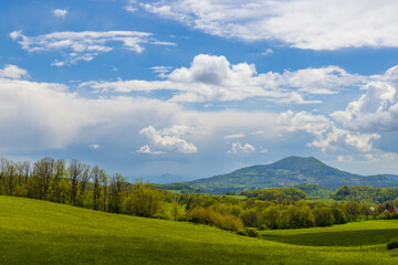 Fototapeta premium Hazmburk Mountain rising above green meadows and trees in Czechia, Ustek