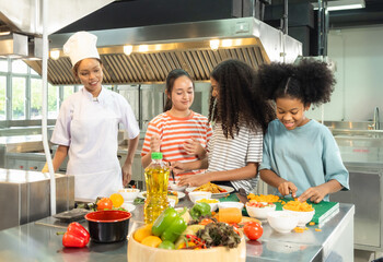 Naklejka premium Kids children cooking group together teamwork happy fun enjoy in class learning clean culinary guid by chef supervision professional in uniform kitchen preparing food with fresh vegetables on counter.