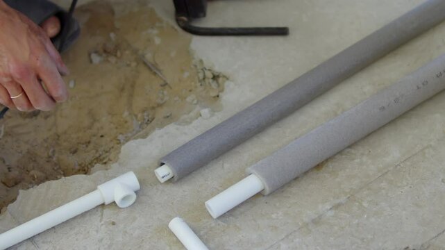 Worker wrapping insulation around plastic pipe on floor