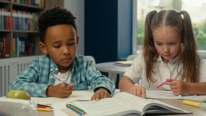 Multiethnic little kids classmates African boy Caucasian girl daughter son elementary school education pupils students children study learn write at desk together schoolgirl schoolboy lesson homework