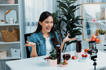 Smiling young beautiful Asian reviewing tasty mixed strawberry and cherry juice detox drinks,...