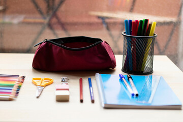 School supplies on a table. Pencils, markers, a ruler, erasers, a notebook, a pen, erasers, and a...