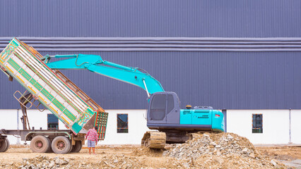 Excavator and trailer truck are working to leveling the ground for the construction site area of a new factory building.