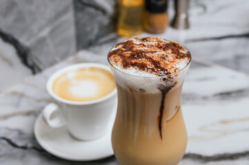 A cup of coffee with a white saucer sits next to a tall glass of chocolate milk