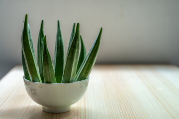 A plate of fresh okra in a bowl on the table. Fresh seasonal ingredient. 