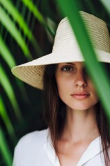 woman with straw hat poses amongst verdant palm fronds in summer