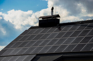 Solar panels cover the roof of a house under a bright sky with fluffy clouds, showcasing renewable...