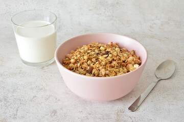 A bowl of granola with a glass of milk and a spoon on gray background