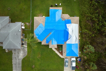Hurricane Ian damaged house rooftop covered with protective plastic tarp against rain water leaking...