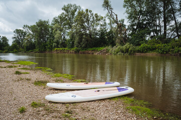A picturesque and serene river scene with vibrant paddle boards resting along the tranquil...