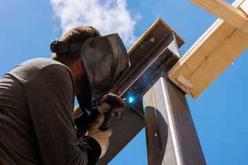 Contractor welds steel beams together at construction site, focusing intently on task while sparks...