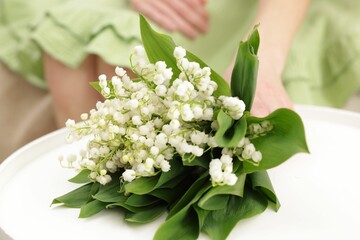 Woman with beautiful lilies of the valley flowers on sofa at table indoors, closeup