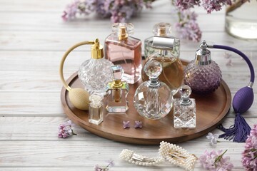 Bottles of perfumes, accessories and lilac flowers on white wooden table