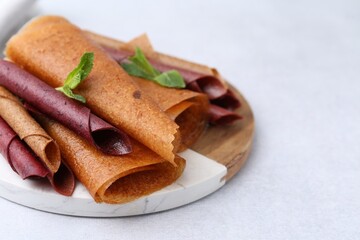 Delicious fruit leather rolls and mint on light table, closeup. Space for text