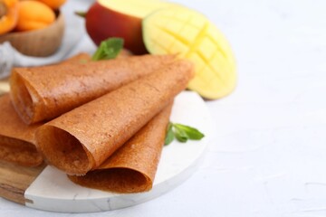 Delicious fruit leather rolls, mint, mango and apricots on white table, closeup. Space for text