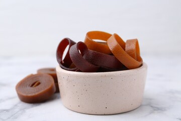 Tasty fruit leather rolls in bowl on white marble table, closeup