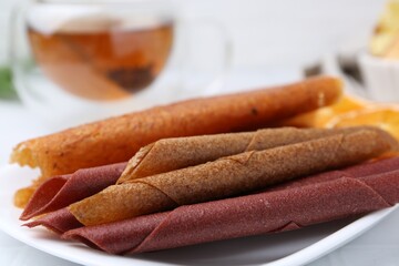 Tasty fruit leather rolls on white table, closeup