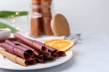 Tasty fruit leather rolls and orange slices on white table. Space for text