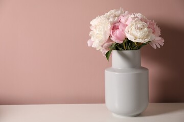 Beautiful peonies in vase on white table near pink wall. Space for text