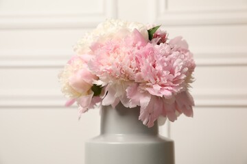 Beautiful peonies in vase near white wall, closeup