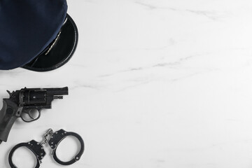 Police cap, gun and handcuffs on white marble table, flat lay. Space for text