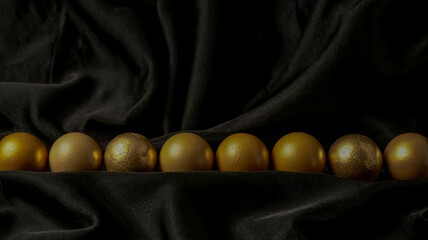A luxurious minimalist scene with identical golden eggs aligned horizontally across a pure black background reflecting warm light in smooth metallic perfection