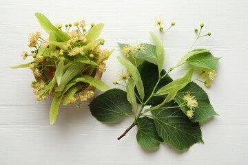 Beautiful linden flowers, leaves and bowl on white wooden table, flat lay