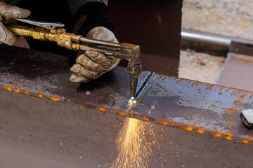 Welder uses torch to cutting metal pieces while sparks fly at construction location under works day