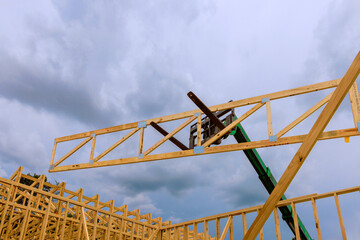 Construction crew operates machinery to raise wooden beams into place amidst overcast skies at...