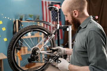 man working to repair bicycle choosing wrench to wheel at home workshop.