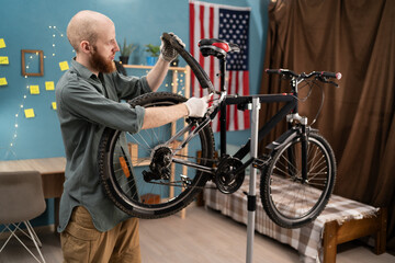 young bearded man repairing bicycle at home attaching fender to wheel