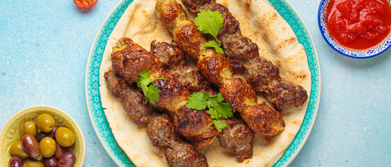 Grilled kofta kebabs are served on pita bread with tomato sauce and garnished with fresh coriander...