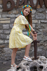 Girl in yellow dress pulling sword from stone, outdoor fairy tale scene