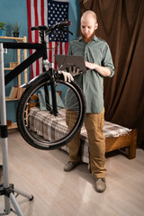 Bearded mechanic doing bike servicing using laptop at home searching replacement components online....