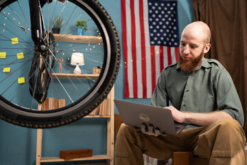 Active cyclist using laptop repair mending his broken bicycle at home. bike maintenance