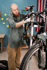 Bearded cyclist in casual clothes repairing bicycle fixing seat standing against american flag at...