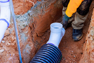 Worker connects drainage pipe trench, ensuring proper installation at construction site under works...