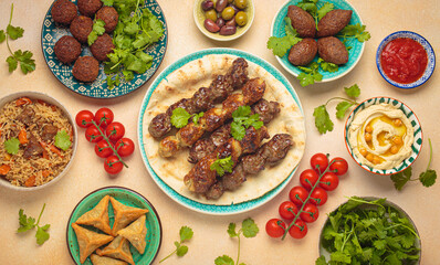 Top view of a vibrant table filled with lebanese dishes and mezze, featuring meat kebabs, falafel, kibbeh, hummus, sambousek, rice, olives. Middle eastern or Arab dishes