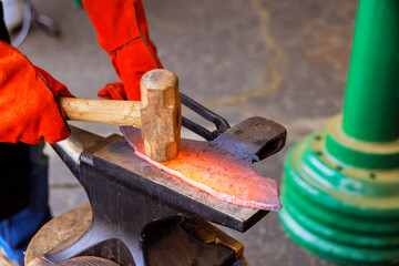 Skilled artisan forges heated metal on an anvil with hammer in during axe making setting.