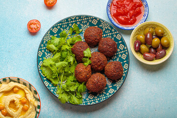 Delicious homemade falafel balls served on a beautiful patterned plate with fresh coriander, tomato sauce and green olives, a vibrant and appetizing middle eastern meal