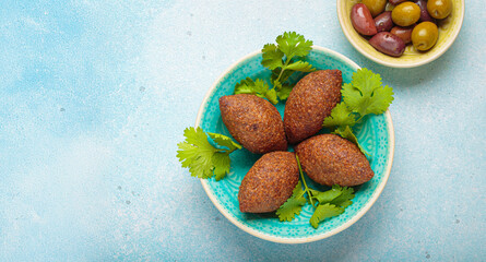 Four kibbeh pieces sit on a turquoise ceramic plate, garnished with fresh cilantro leaves, middle eastern cuisine top view on light beige background, copy space