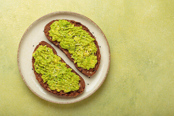 Mashed avocado seasoned with sesame seeds is spread on two slices of toasted rye bread, served on a...